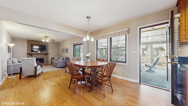 dining room with ceiling fan, a fireplace, baseboards, and light wood-style floors