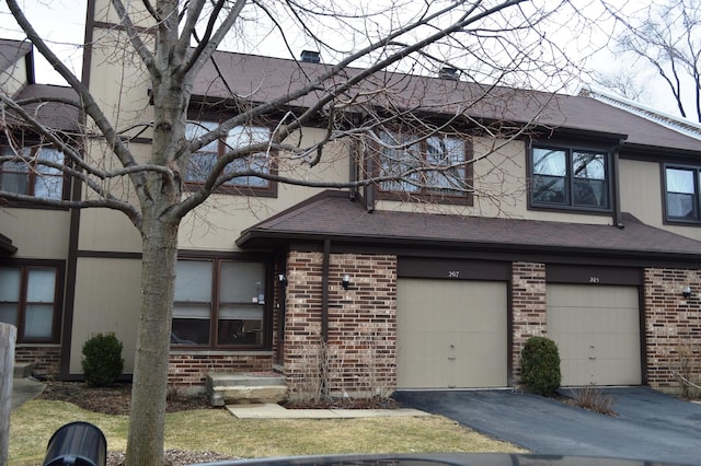 view of front of house featuring aphalt driveway, a garage, brick siding, and roof with shingles