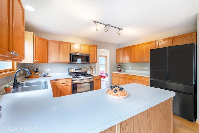 kitchen with appliances with stainless steel finishes, a sink, light countertops, a peninsula, and light wood-style flooring