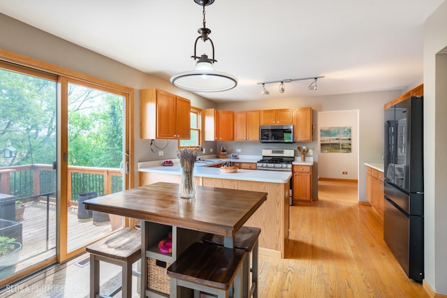 kitchen with stainless steel appliances, light countertops, light wood-style floors, a sink, and hanging light fixtures