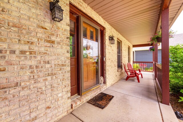 doorway to property with a porch and brick siding