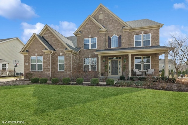 traditional-style home with brick siding, a porch, roof with shingles, and a front yard