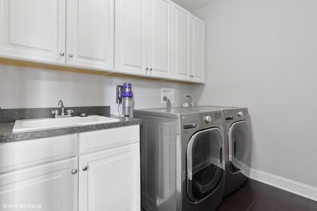 washroom featuring a sink, washer and dryer, cabinet space, baseboards, and dark wood-type flooring