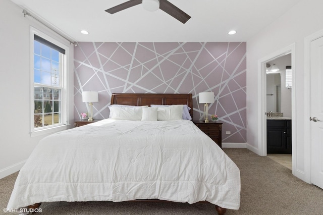 carpeted bedroom with a sink, baseboards, an accent wall, a ceiling fan, and ensuite bath