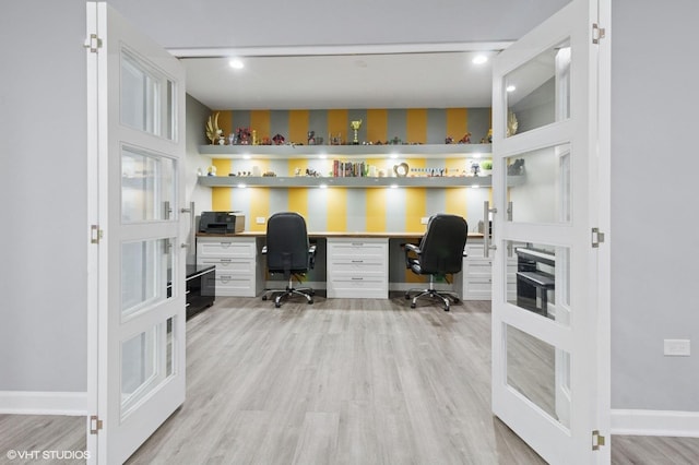 home office with built in study area, baseboards, french doors, and light wood-style floors
