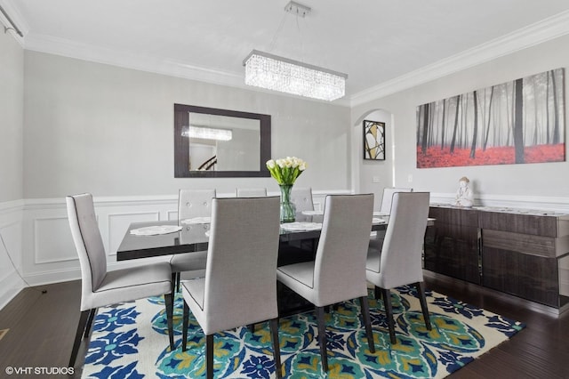 dining room with wood finished floors, ornamental molding, arched walkways, wainscoting, and a chandelier