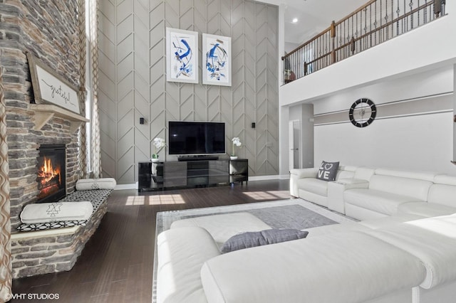 living area with an accent wall, a stone fireplace, a towering ceiling, wood-type flooring, and baseboards