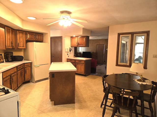 kitchen with a ceiling fan, a center island, white appliances, brown cabinetry, and light countertops