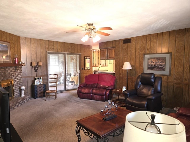 carpeted living area with a brick fireplace, visible vents, wood walls, and ceiling fan