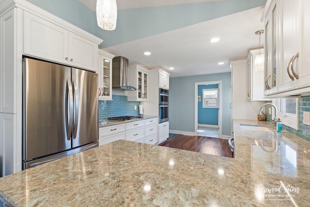 kitchen featuring light stone countertops, a sink, decorative backsplash, stainless steel appliances, and wall chimney range hood