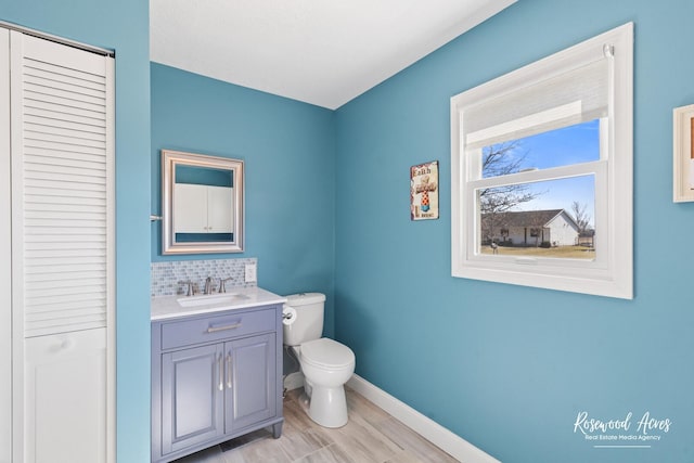 bathroom with vanity, baseboards, a closet, toilet, and tasteful backsplash