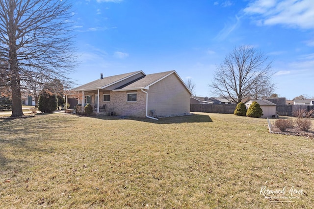 rear view of property featuring brick siding, fence, a shed, a lawn, and an outbuilding