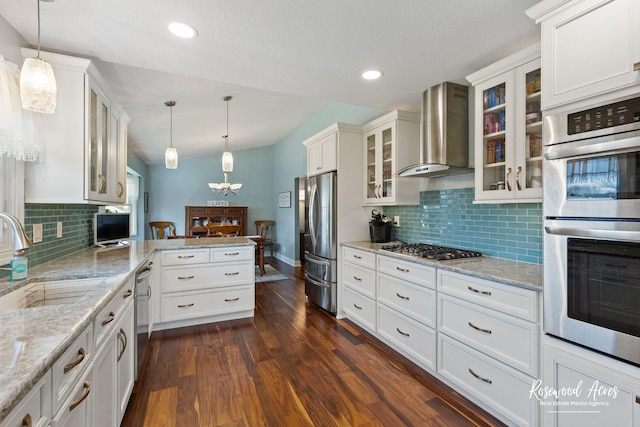 kitchen featuring dark wood-style floors, a peninsula, a sink, appliances with stainless steel finishes, and wall chimney range hood