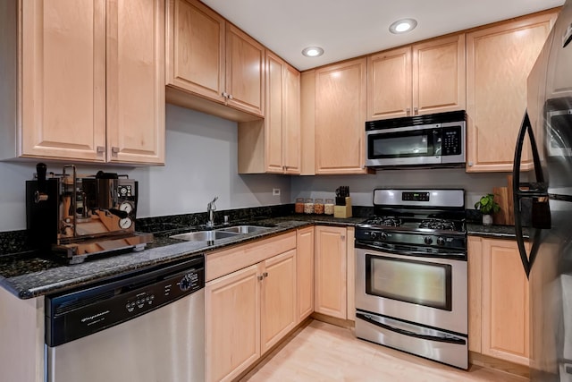 kitchen with stainless steel appliances, a sink, light brown cabinets, recessed lighting, and dark stone counters
