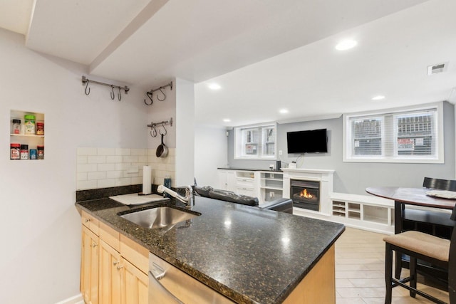 kitchen with light brown cabinets, visible vents, a lit fireplace, decorative backsplash, and a sink