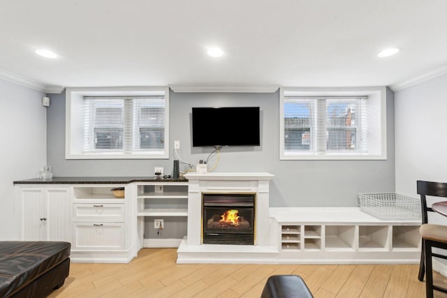 living area featuring a glass covered fireplace, crown molding, recessed lighting, and light wood-type flooring