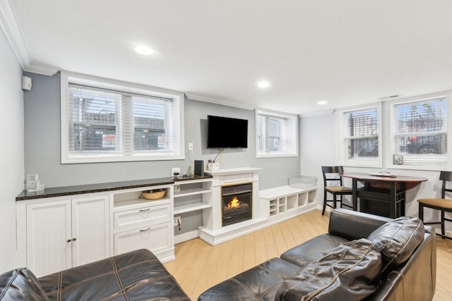 living room with crown molding, light wood finished floors, recessed lighting, and a warm lit fireplace