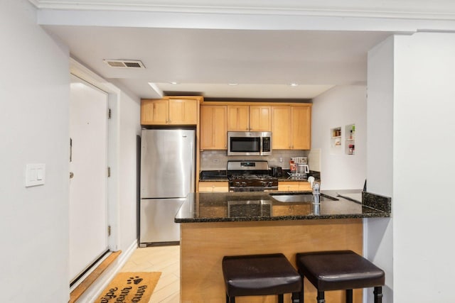 kitchen with a sink, dark stone countertops, backsplash, appliances with stainless steel finishes, and a peninsula