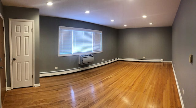 unfurnished room featuring baseboards, baseboard heating, an AC wall unit, and wood finished floors