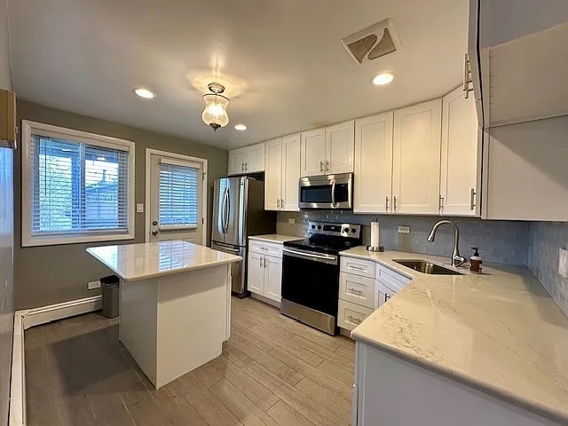 kitchen featuring tasteful backsplash, visible vents, a kitchen island, stainless steel appliances, and a sink