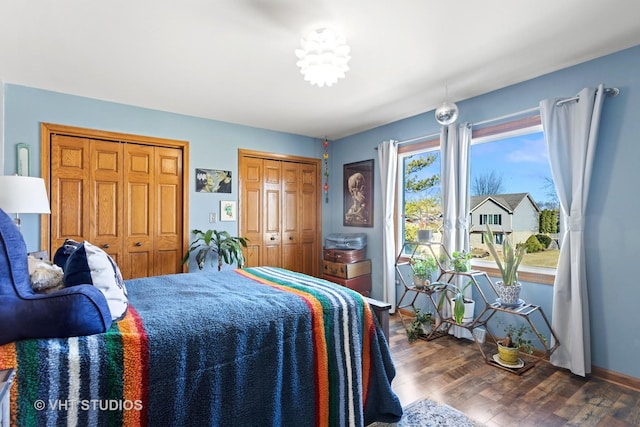 bedroom with wood finished floors, baseboards, and two closets