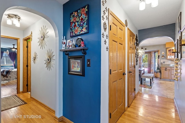 corridor featuring a textured ceiling, light wood-style floors, arched walkways, and baseboards