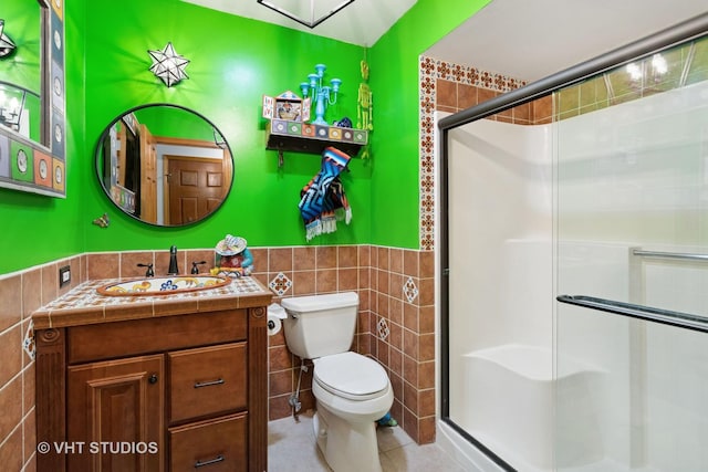 full bath featuring toilet, tile walls, wainscoting, a shower stall, and vanity