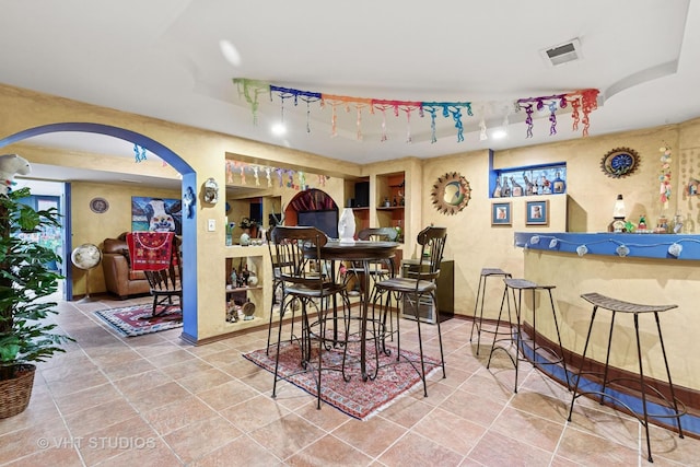 dining room featuring visible vents, baseboards, a tray ceiling, arched walkways, and a bar