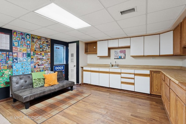 kitchen featuring visible vents, a drop ceiling, light countertops, light wood-style floors, and a sink