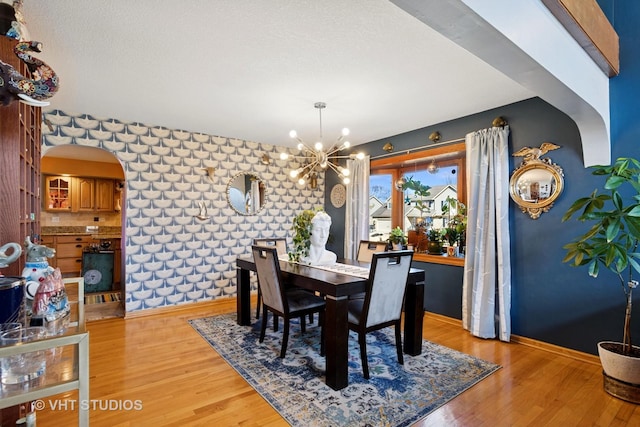 dining space featuring light wood-style flooring, a textured ceiling, arched walkways, an inviting chandelier, and baseboards