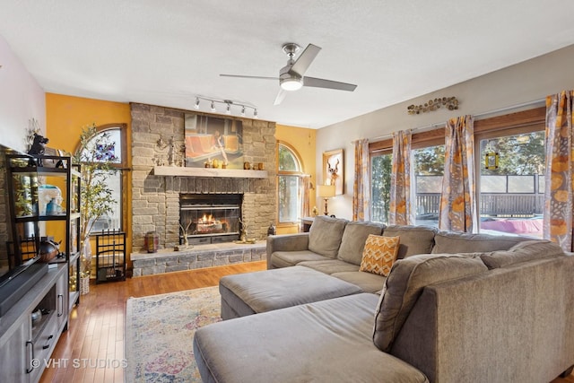 living room with a stone fireplace, a ceiling fan, and hardwood / wood-style floors