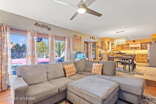 living area featuring light wood-style flooring and ceiling fan with notable chandelier