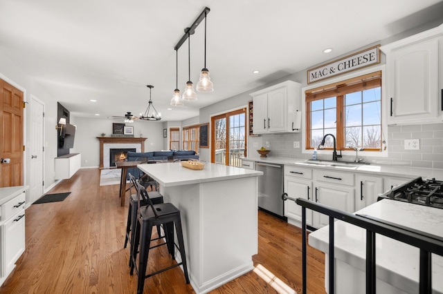 kitchen featuring a center island, dishwasher, a warm lit fireplace, white cabinetry, and a sink