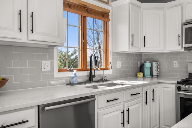 kitchen with tasteful backsplash, light stone countertops, stainless steel appliances, white cabinetry, and a sink