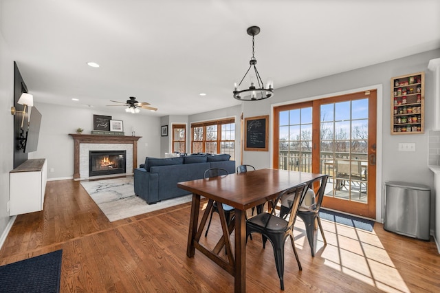 dining room with recessed lighting, a glass covered fireplace, ceiling fan with notable chandelier, and wood finished floors