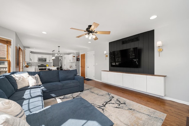 living area featuring wood finished floors, recessed lighting, ceiling fan with notable chandelier, and baseboards