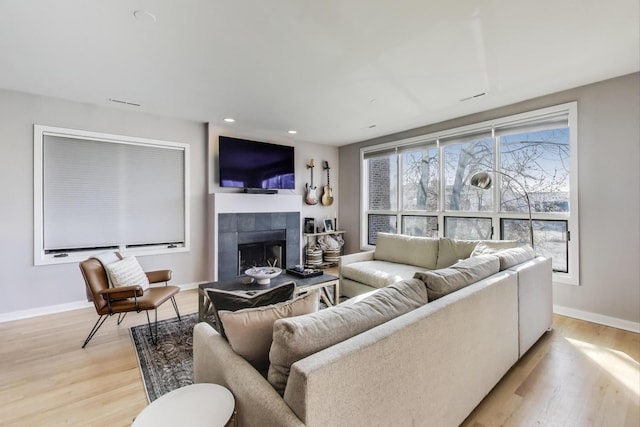 living area with a tile fireplace, light wood-type flooring, and baseboards