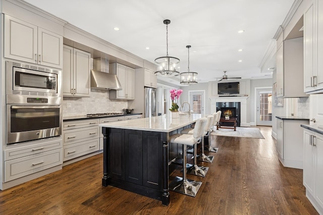 kitchen with ornamental molding, open floor plan, appliances with stainless steel finishes, wall chimney exhaust hood, and tasteful backsplash