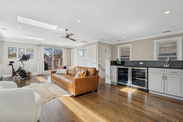 living area with beverage cooler, visible vents, ornamental molding, and wood finished floors