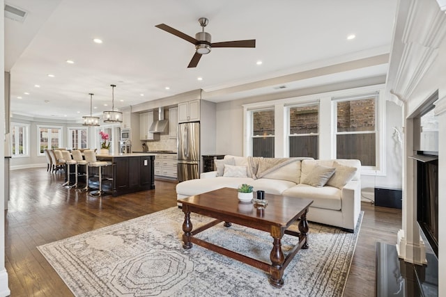 living area with visible vents, crown molding, ceiling fan with notable chandelier, recessed lighting, and dark wood-style floors