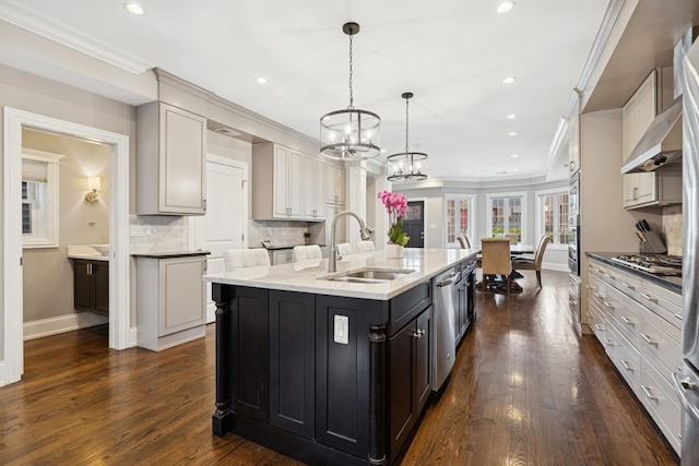 kitchen with a kitchen island with sink, ornamental molding, a sink, backsplash, and stainless steel appliances