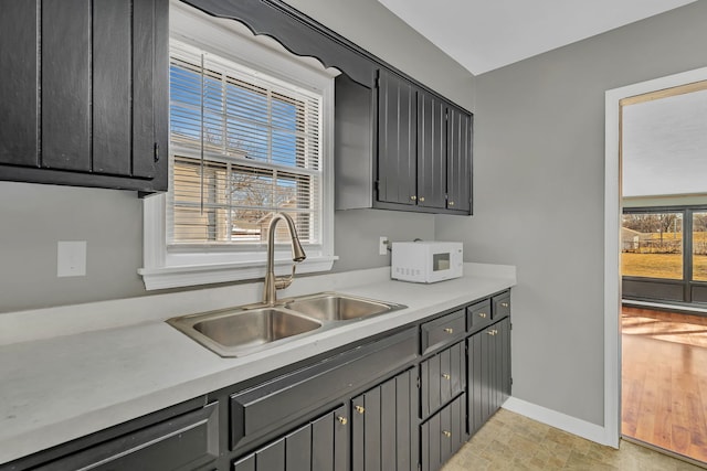 kitchen with a sink, baseboards, white microwave, and light countertops