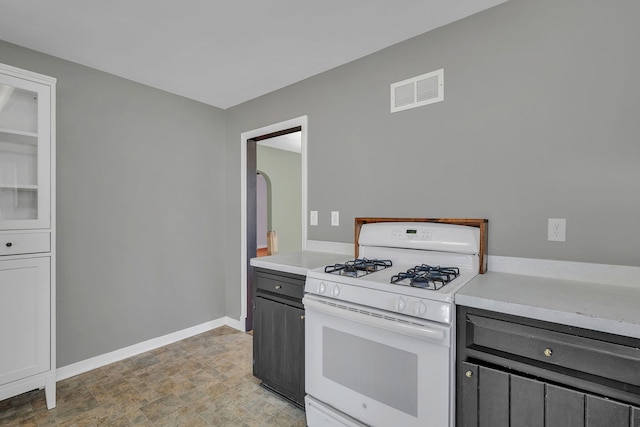 kitchen with visible vents, white gas range oven, arched walkways, light countertops, and baseboards