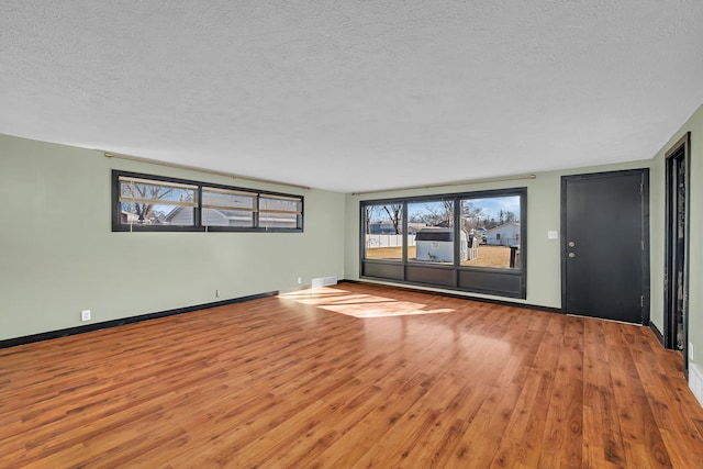 empty room featuring visible vents, baseboards, a textured ceiling, and wood finished floors