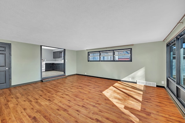 unfurnished living room with light wood finished floors, visible vents, a textured ceiling, and baseboards