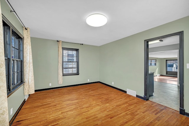 empty room with plenty of natural light, wood finished floors, visible vents, and baseboards