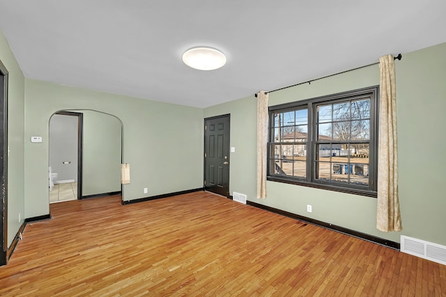 empty room featuring visible vents, arched walkways, and light wood-style floors