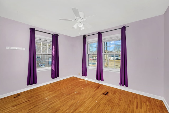 spare room featuring a ceiling fan, plenty of natural light, wood finished floors, and baseboards