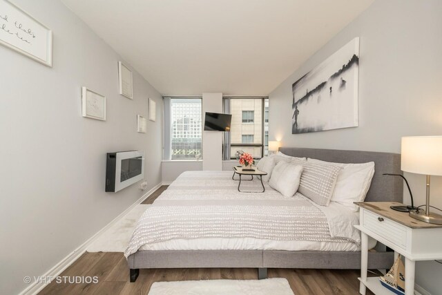 bedroom featuring heating unit, baseboards, and wood finished floors