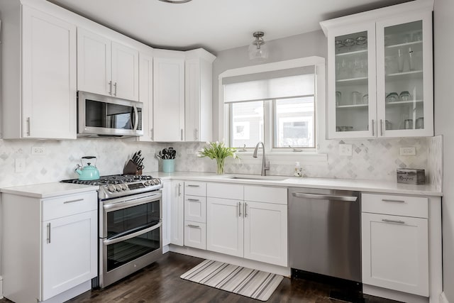 kitchen with a sink, stainless steel appliances, white cabinets, light countertops, and glass insert cabinets